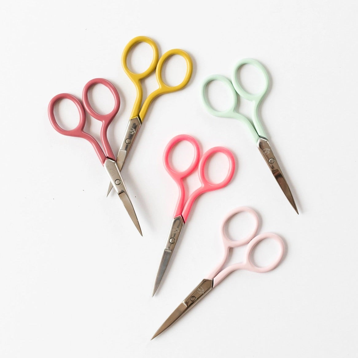 Five pairs of scissors with pastel-colored handles in pink, yellow, mint green, coral pink, and light pink, arranged on a clean white background.